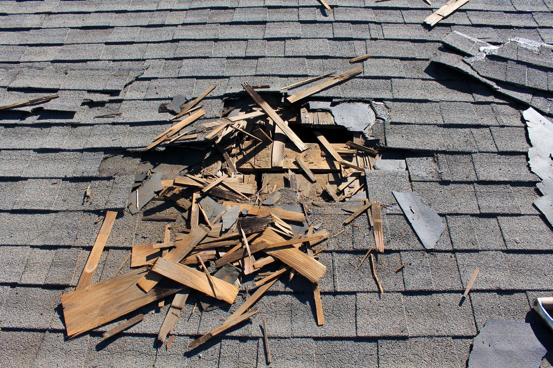 Damaged asphalt shingle roof with a large hole and scattered debris.