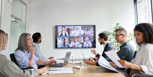 Group of people in a conference room with a video call on a screen.